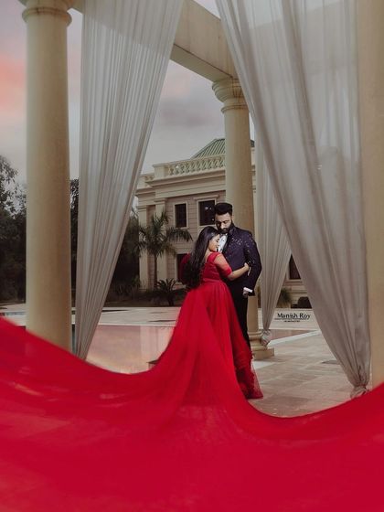 A dramatic pre-wedding shot with a flowing red gown. The makeup is bold and captivating to match the drama of the outfit and the grand setting.
