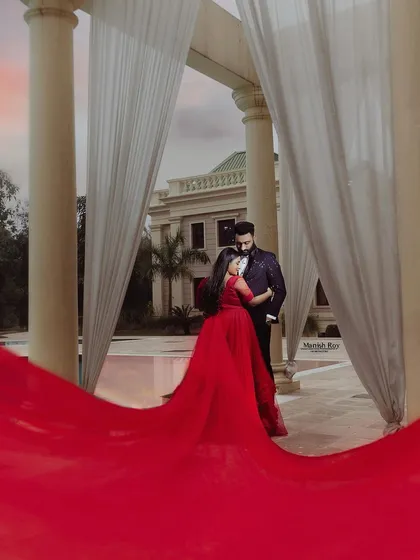 A dramatic pre-wedding shot with a flowing red gown. The makeup is bold and captivating to match the drama of the outfit and the grand setting.