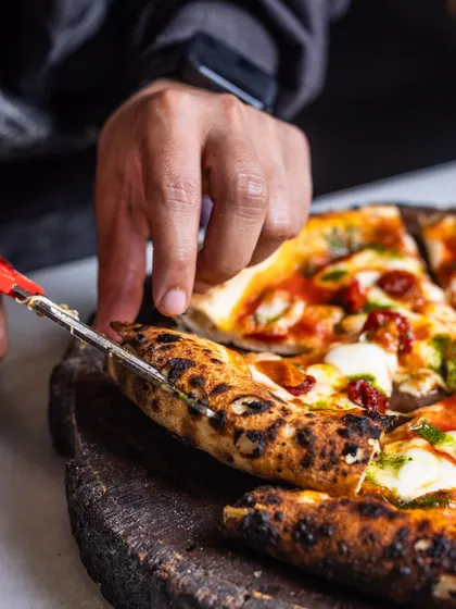 Using scissors to cut pizza is a traditional Italian way to preserve the integrity of the crust and toppings. Here, we're slicing up our Sundried Tomato & Basil pizza.