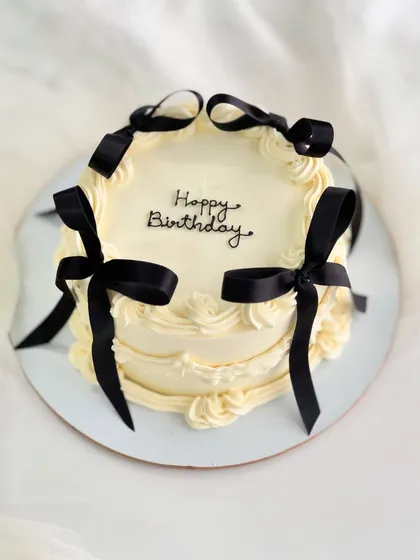 A vintage-style cake with a modern twist, featuring delicate piping and bold black ribbons. This design is a favorite for chic birthday celebrations.