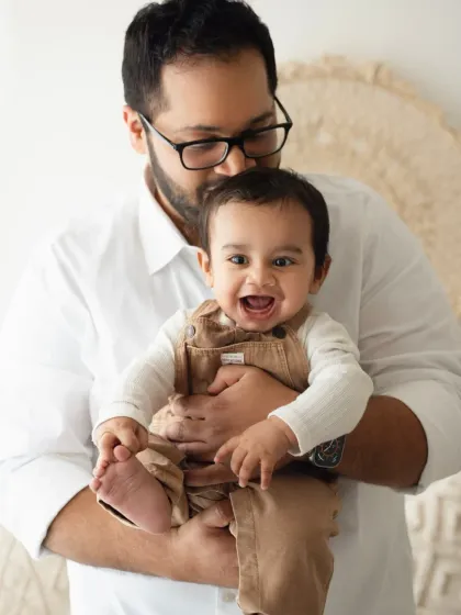 A proud father holds his laughing baby boy. This portrait is full of joy and captures a beautiful father-son bond.