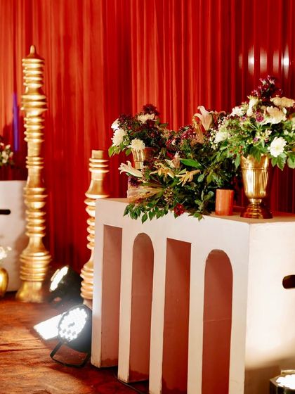 Decorative details for the red-themed reception, including large golden finials and modern white consoles holding lush floral arrangements.