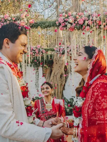 A moment of shared laughter between the couple during their ceremony. The backdrop of pink flowers and hanging floral strings adds to the romance and joy of the occasion.