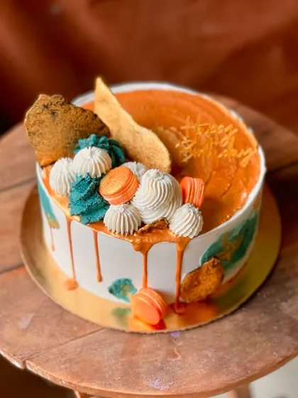 An abstract, artistic cake with a caramel drip, macarons, and textured buttercream.