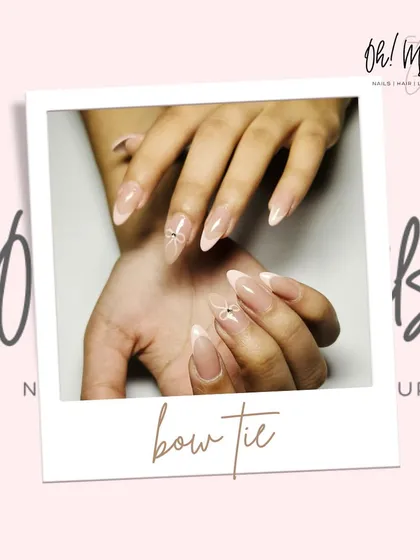 Bows aren't just for gifts. This elegant set features a classic French manicure on long, almond-shaped nails, with a delicate crystal bow accent for a touch of sparkle.