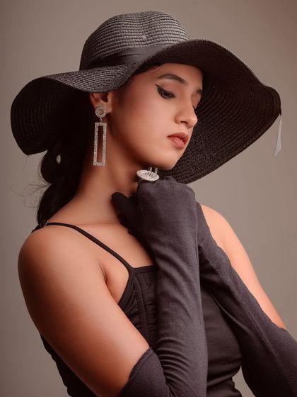 A classic, elegant portrait of a model in a black dress and hat. The pose and styling evoke a sense of timeless Hollywood glamour.