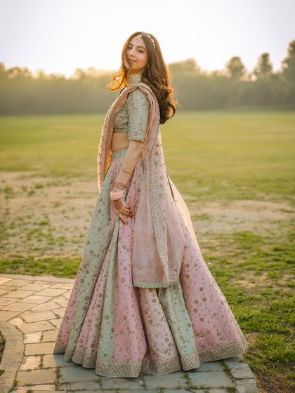 A full-length portrait of a bride in a pastel lehenga, bathed in the warm glow of the setting sun.