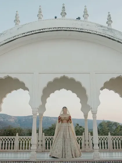 A breathtaking wide shot of the bride standing in a white marble pavilion at Nahargarh Palace, with the Aravalli hills providing a stunning backdrop.