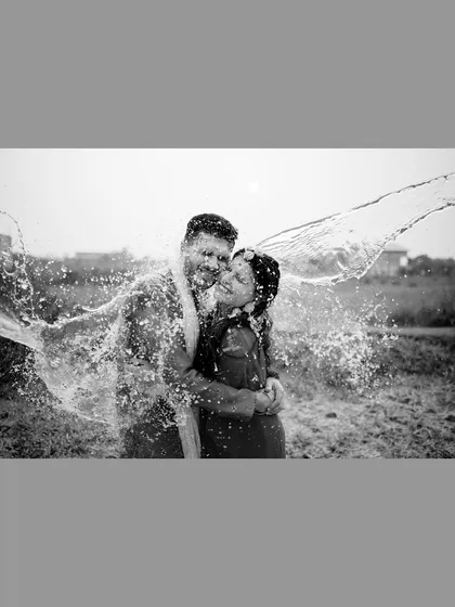 A playful black and white shot of the couple getting drenched with water during their outdoor Haldi celebration.
