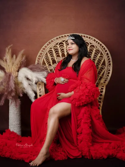 Regal in red. Seated on our wicker throne chair, this mom-to-be exudes confidence and glamour in a stunning red gown and tiara.