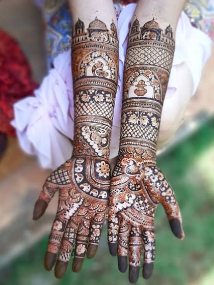 A traditional bridal mehendi with palace and elephant motifs on the arms. The palms are filled with a mix of floral and paisley patterns for a classic look.