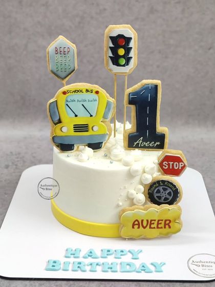 A cute school bus cake for a first birthday. This cake is decorated with cookie toppers shaped like a bus, traffic lights, and road signs.
