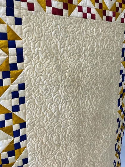 A close-up of the cream-colored center, filled with a dense, swirling free-motion quilting pattern.