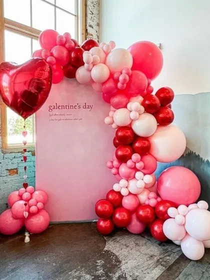 This "Galentine's Day" photo booth features a beautiful balloon arch in shades of pink and red against a simple pink backdrop. The large heart-shaped foil balloon adds a classic romantic touch.