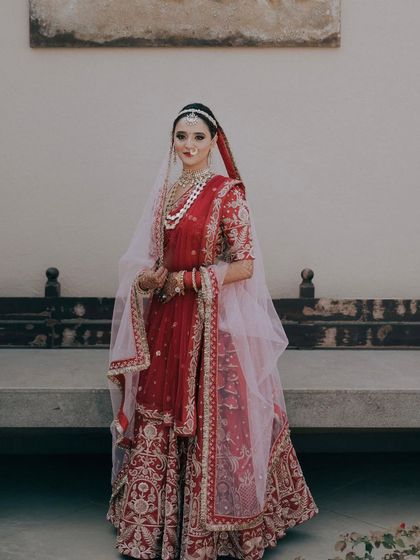 A full-length portrait of the bride in her traditional red lehenga. Her pose is graceful and poised, a perfect picture of a classic Indian bride.