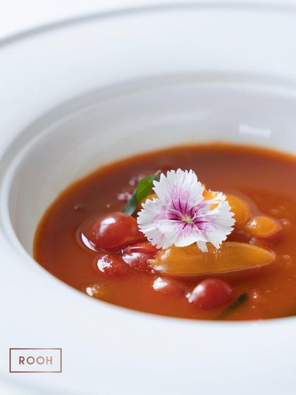 A close-up of the Cherry Tomato Rasam, garnished with an edible flower. It's a modern interpretation of a South Indian classic, bursting with fresh, zesty flavour.