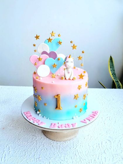 A sweet unicorn-themed first birthday cake with a pink and blue ombre effect, decorated with stars and hearts.