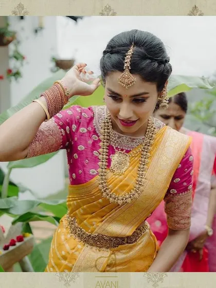 A bride in a yellow Kanchipuram saree with a contrasting pink blouse. The blouse is heavily embroidered, making it a standout piece of her bridal ensemble.