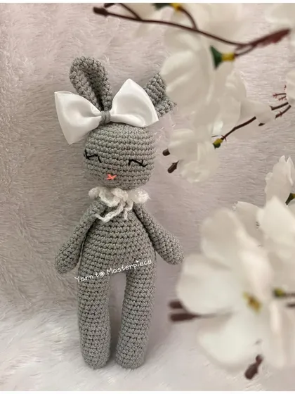 An elegant and sleepy-eyed bunny doll, this amigurumi is made in a chic grey yarn and finished with a large white satin bow.