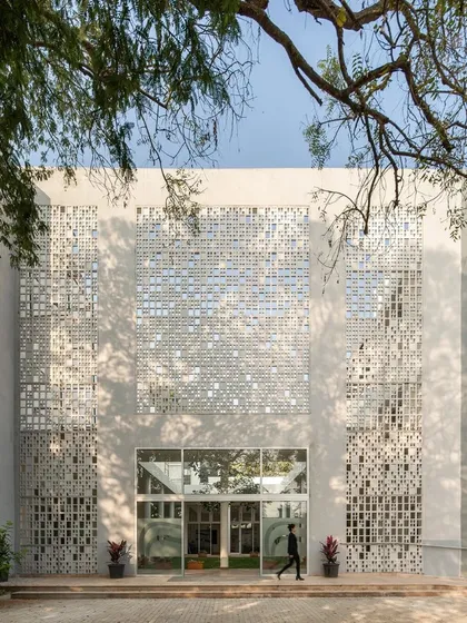 The facade of Vidyashilp Academy, seen through the branches of a tree, emphasizes the harmony between the built and natural environments. The 'jaali' screens provide a textured, permeable skin for the building.