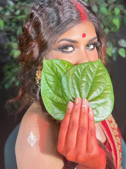 A traditional Bengali bridal look, featuring the "paan pata" held to the face. The saree is draped perfectly to showcase its beauty.