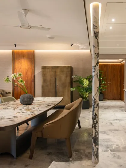 The design language of marble and wood flows seamlessly from the living room to the dining area in this balanced home. Bespoke lighting and a freestanding marble partition draw attention to the dining surface, heightening its theatrical presence.
