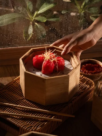A hand reaching for a vibrant red beet dumpling. The color contrast and human interaction make this an engaging photo.