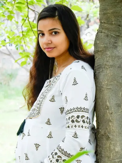 A beautiful portrait of a mother-to-be leaning against a tree. The natural green background makes the subject stand out.