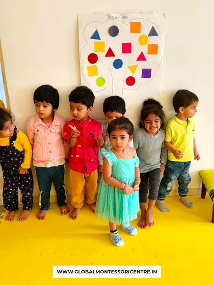 Our proud playgroup students stand by their completed 'shapes tree' activity board, showcasing their collective effort and learning.