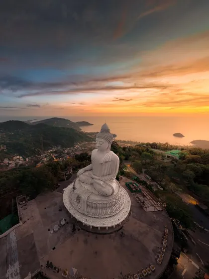 A wide panoramic shot of the Big Buddha statue overlooking the coastline of Phuket at sunset. The view from here is absolutely breathtaking.
