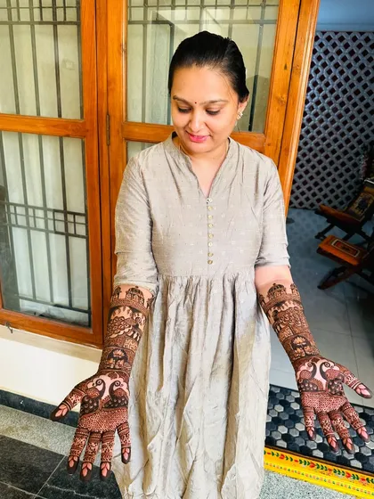 A proud client displaying her stunningly intricate mehndi, which features architectural and peacock designs from her palms to her elbows.