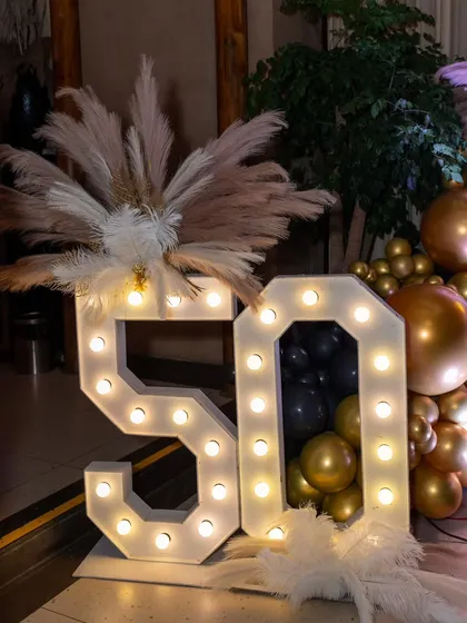 Large light-up '50' marquee numbers surrounded by pampas grass and balloons. These are a popular and impactful centerpiece for any milestone birthday.