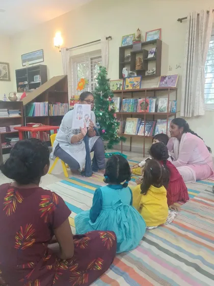 The storyteller shows illustrations from a Christmas book, with the decorated tree visible in the background.