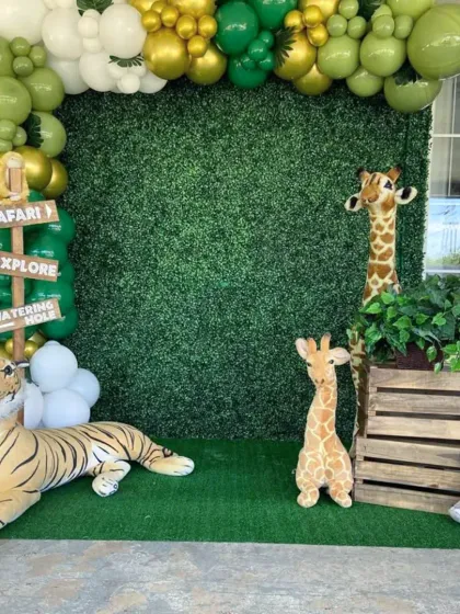 For this safari-themed party, I used a green hedge backdrop, a balloon arch in shades of green and gold, and large plush animals like a tiger and giraffe to create an exciting atmosphere.