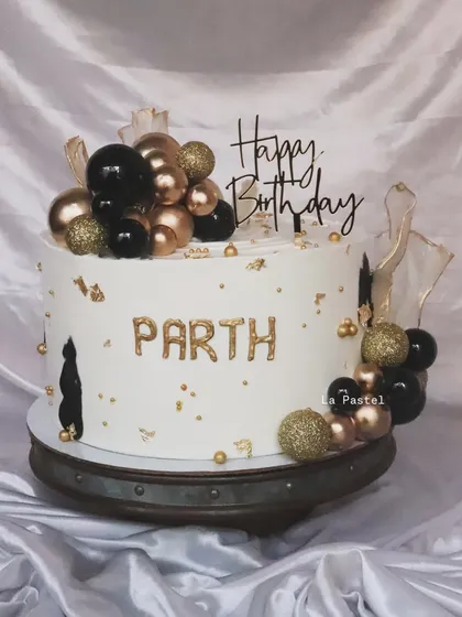 A bold and stylish cake perfect for a milestone birthday. The black and gold balloon clusters create a striking contrast against the white cake, personalized with a name in gold.