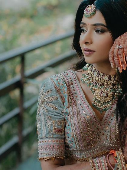 A classic three-quarter portrait of Ipsa in a natural outdoor setting. The warm sunlight highlights her features and the delicate embroidery of her pastel lehenga.