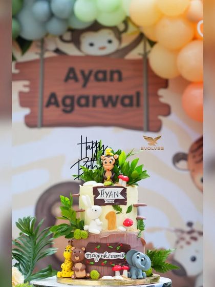 Another view of the jungle-themed cake and backdrop for Ayan's birthday, showing the cute animal characters and pastel balloon arch.