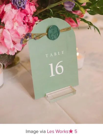 A custom table number I designed, featured on the WedMeGood blog. The arched card in sage green is adorned with a custom wax seal and dried flowers for a rustic yet elegant look.