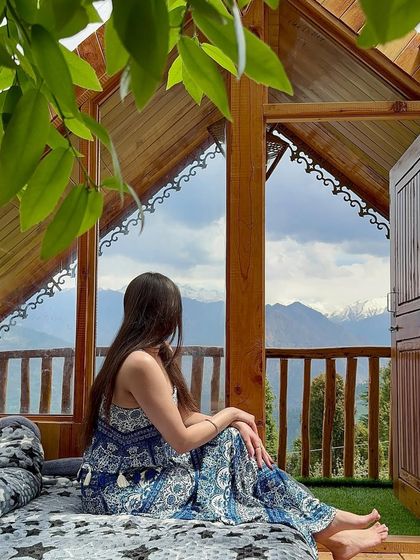 A peaceful moment in a treehouse with a breathtaking mountain view. I'm wearing a comfortable and stylish blue printed jumpsuit, perfect for a relaxed getaway.