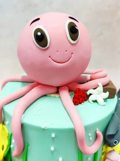 A close-up of our friendly pink octopus cake topper, with big, curious eyes and a happy smile.