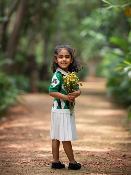A sweet girl holding a bouquet of yellow flowers on a path in the woods. Her preppy outfit and the natural surroundings make for a timeless child portrait.