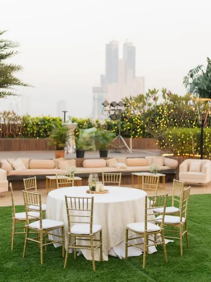 An outdoor reception setup with a mix of lounge seating and round tables, overlooking the city skyline.
