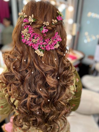 The back view of this stunning Mehendi hairstyle. A half-up braided look is heavily adorned with intricate pink floral accessories and scattered pearls.