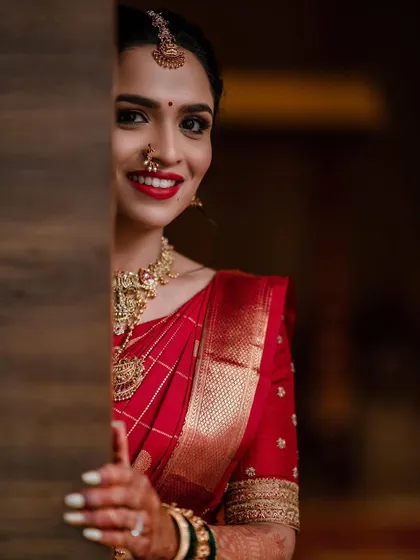 A candid shot of a bride in her red saree, showcasing her bright smile and the timeless elegance of her custom-designed blouse.