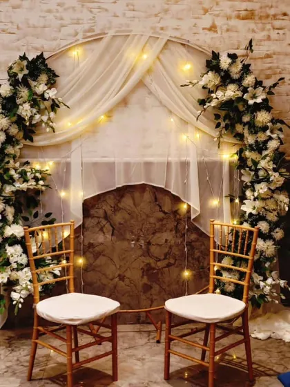 A simple and elegant setup for an intimate ring ceremony or home engagement. We used a circular arch decorated with white flowers and sheer drapes, illuminated by fairy lights to create a warm and romantic photo corner.