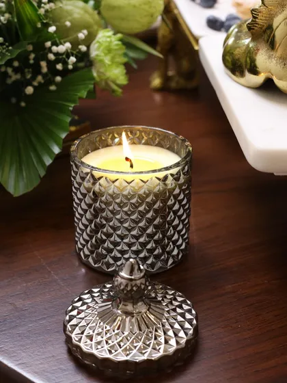 The smoke grey Crystal Cove candle, with its lid removed, casting a warm glow. The diamond-cut glass beautifully reflects the light, adding to its serene charm.