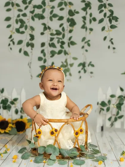 A 7-month-old baby girl beams with a huge smile, sitting in a basket surrounded by sunflowers. This setup is perfect for capturing the bright and cheerful personality of a sitter.