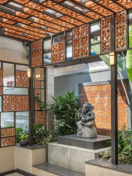 A tranquil outdoor alcove designed for a Ganesha statue. The space uses a combination of terracotta jali screens, laterite stone, and lush greenery to create a modern yet sacred-feeling shrine.