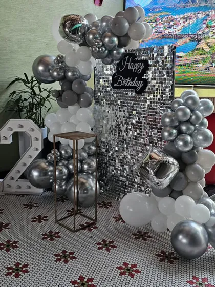 A chic and modern 12th birthday party setup with a silver and white theme, featuring a sequin backdrop and a metallic balloon garland.