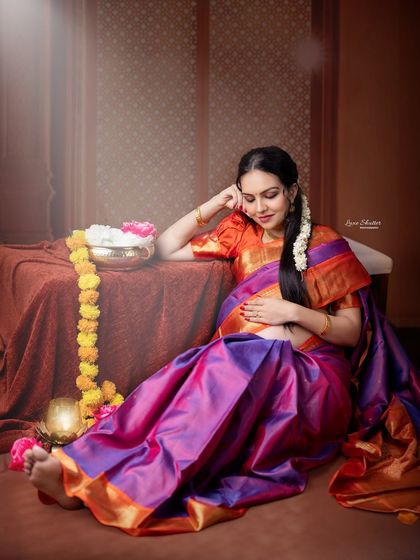 A quiet moment of reflection for the mother-to-be. Dressed in a stunning silk saree, she relaxes in a beautifully styled traditional setting with flowers and a brass lamp.